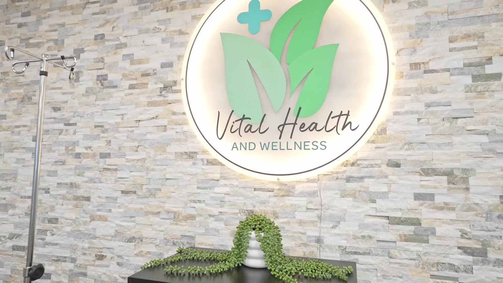 The illuminated Vital Health and Wellness logo on the stone lobby wall of the Woodlawn, Virginia clinic